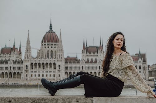 A woman sitting on a wall in front of the hungarian parliament building