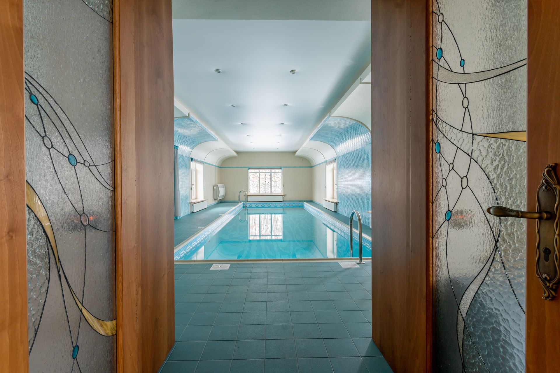Elegant indoor swimming pool with stained glass doors, perfect for luxury relaxation.