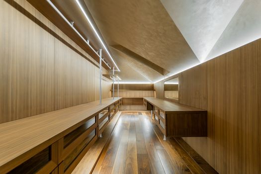 Spacious contemporary walk-in closet with sleek wooden design and ambient lighting.