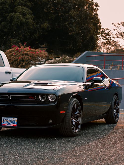 Free A black Dodge Charger parked outdoors, reflecting golden sunset hues, showcasing its sleek design. Stock Photo
