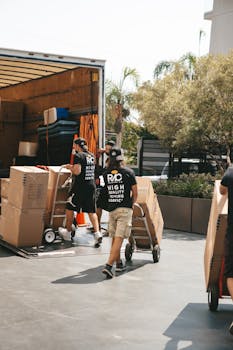 Movers loading boxes into a truck on a sunny day, capturing a busy urban scene.