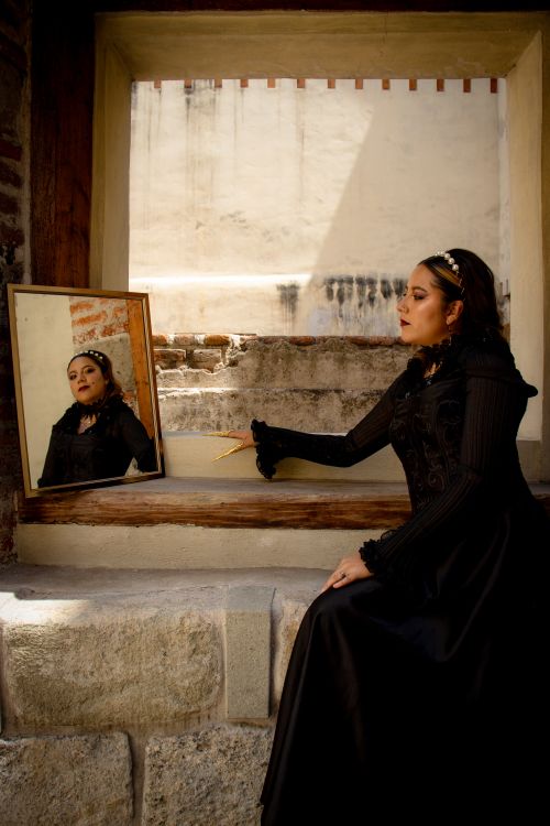 Free A woman in a black dress gazes at her reflection in a mirror against a textured urban backdrop. Stock Photo