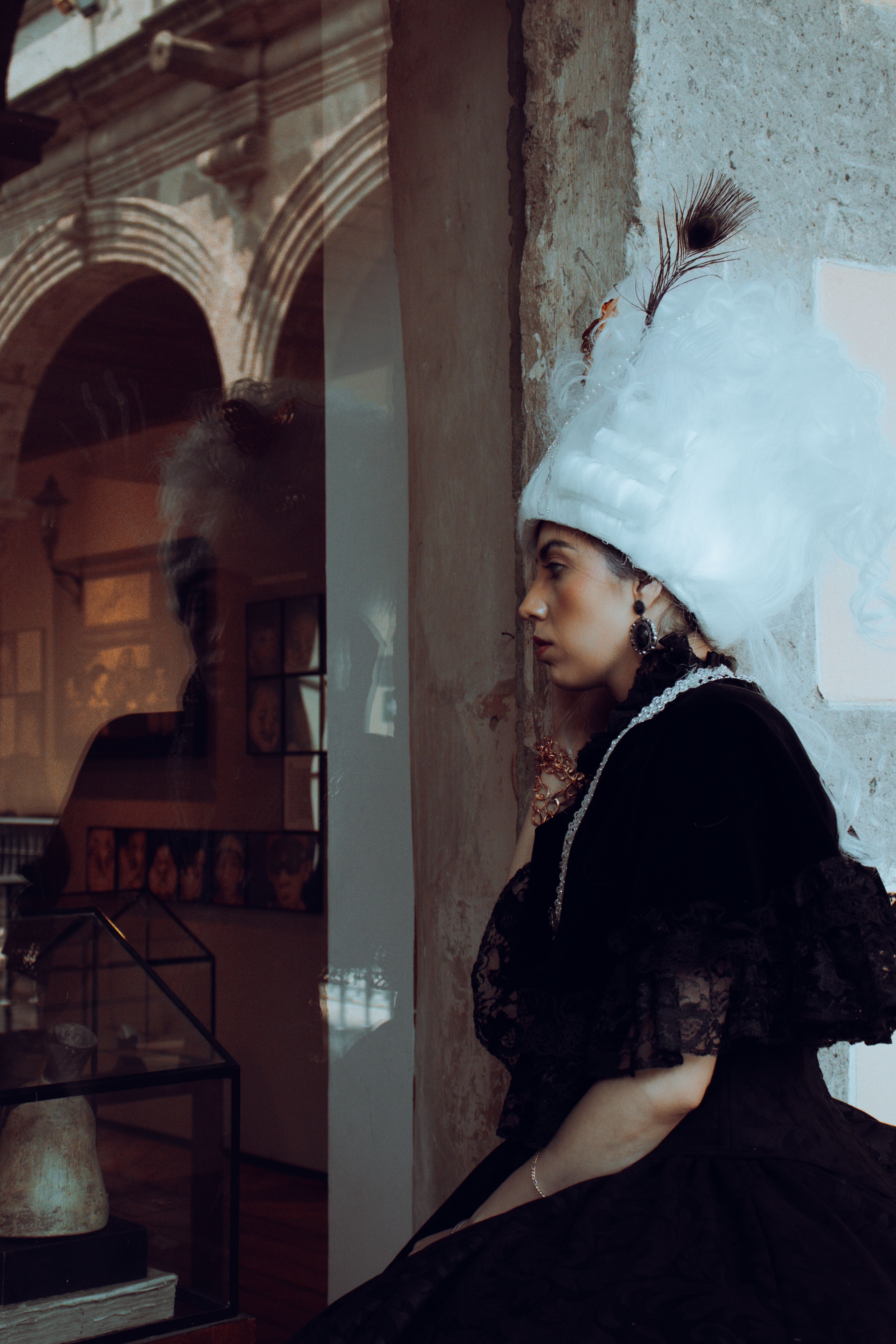 Woman in vintage attire with white hat and black dress gazing out window in Mexico City.