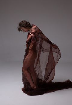 A woman artistically posed in sheer fabric, studio photography.
