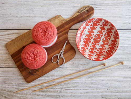 Two Pink Spools on Brown Wooden Chopping Board Beside Orange Bowl 