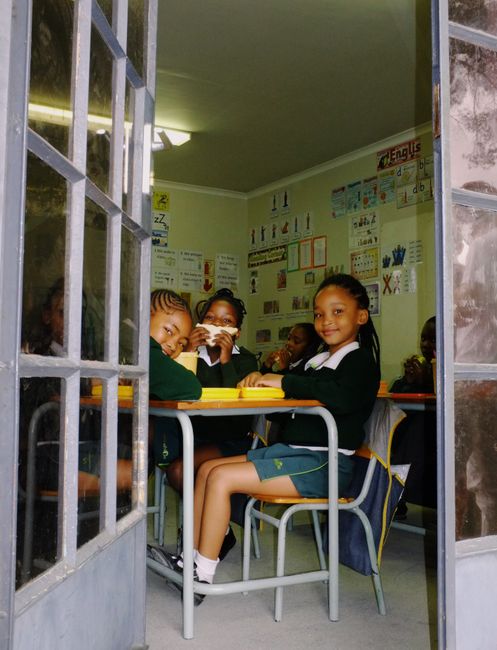Young students sitting in classroom enjoying lunch, surrounded by educational materials.