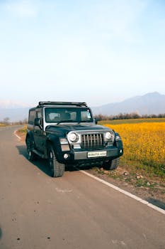 4x4 SUV parked on a rural road beside vibrant yellow fields with mountains in the background.