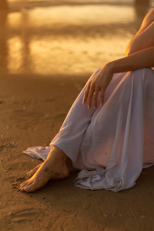 Free Legs of Woman in White Dress Sitting on Beach Stock Photo