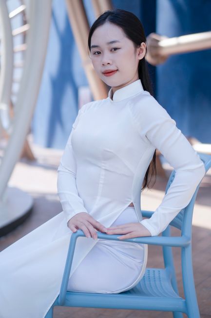 Young woman in a white Ao Dai, elegantly sitting on a chair outdoors.
