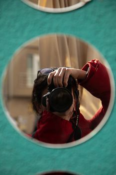 Artistic reflection photo capturing a photographer in a red jacket using a Canon camera.