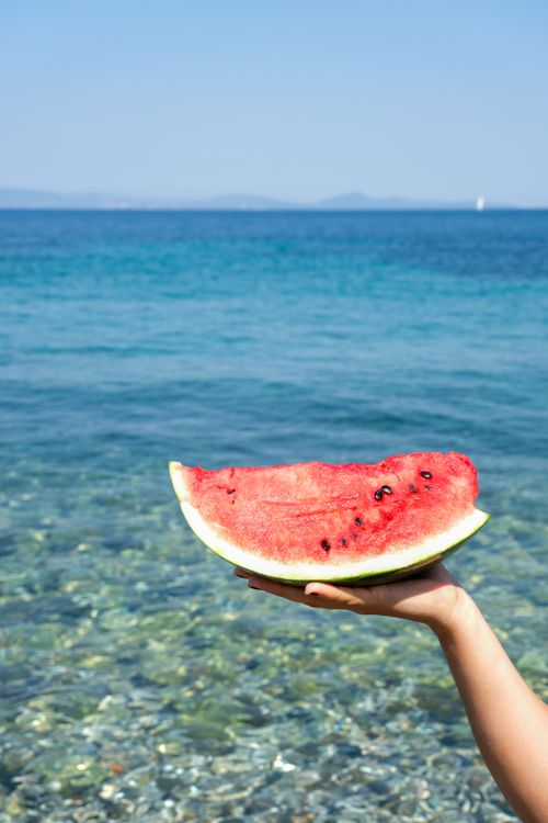 Free Juicy watermelon slice held by the sea, capturing summer vibes and relaxation. Stock Photo