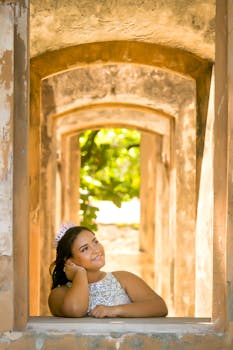 A woman in a crown smiles thoughtfully while leaning on a rustic window in Puerto Plata, Dominican Republic.