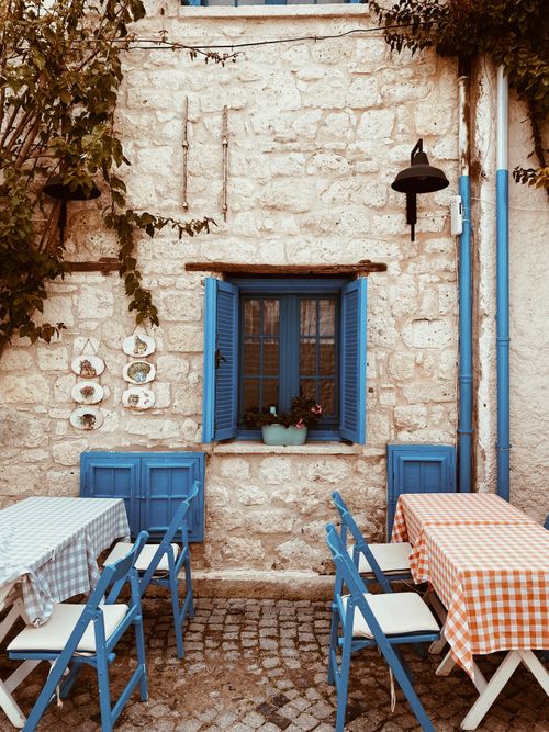 Free Charming outdoor cafe in Alaçatı, Türkiye with blue accents and checkered tablecloths, ideal for a relaxed meal. Stock Photo
