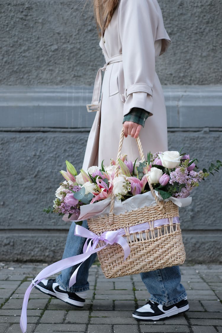 Woman Holding A Straw Basket With Flowers On A Street 