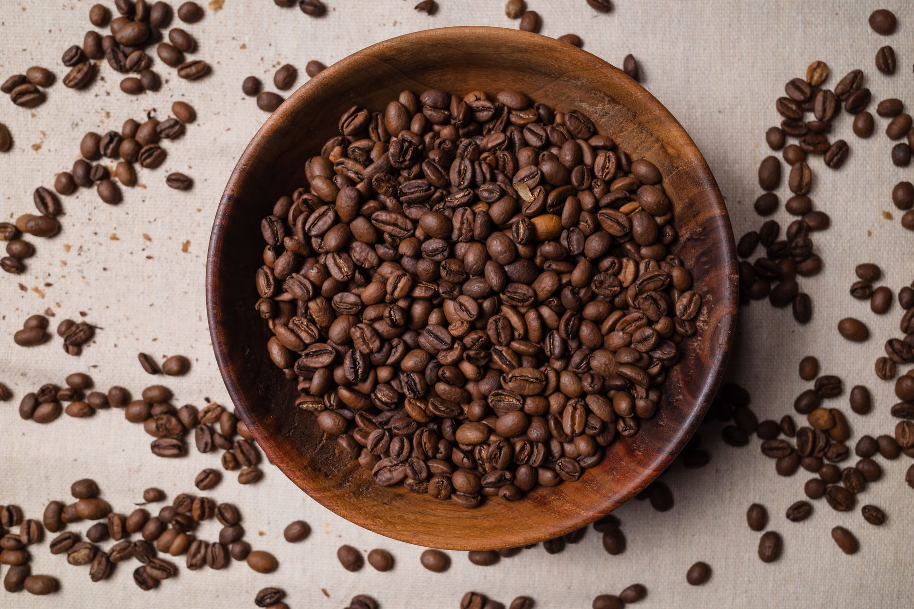 Top view of coffee beans in a wooden bowl on a textured surface, showcasing abundance and texture.