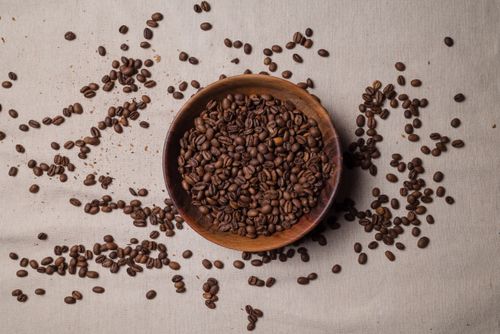 Free Aerial shot of roasted coffee beans in a wooden bowl on a textile surface, perfect for food photography. Stock Photo