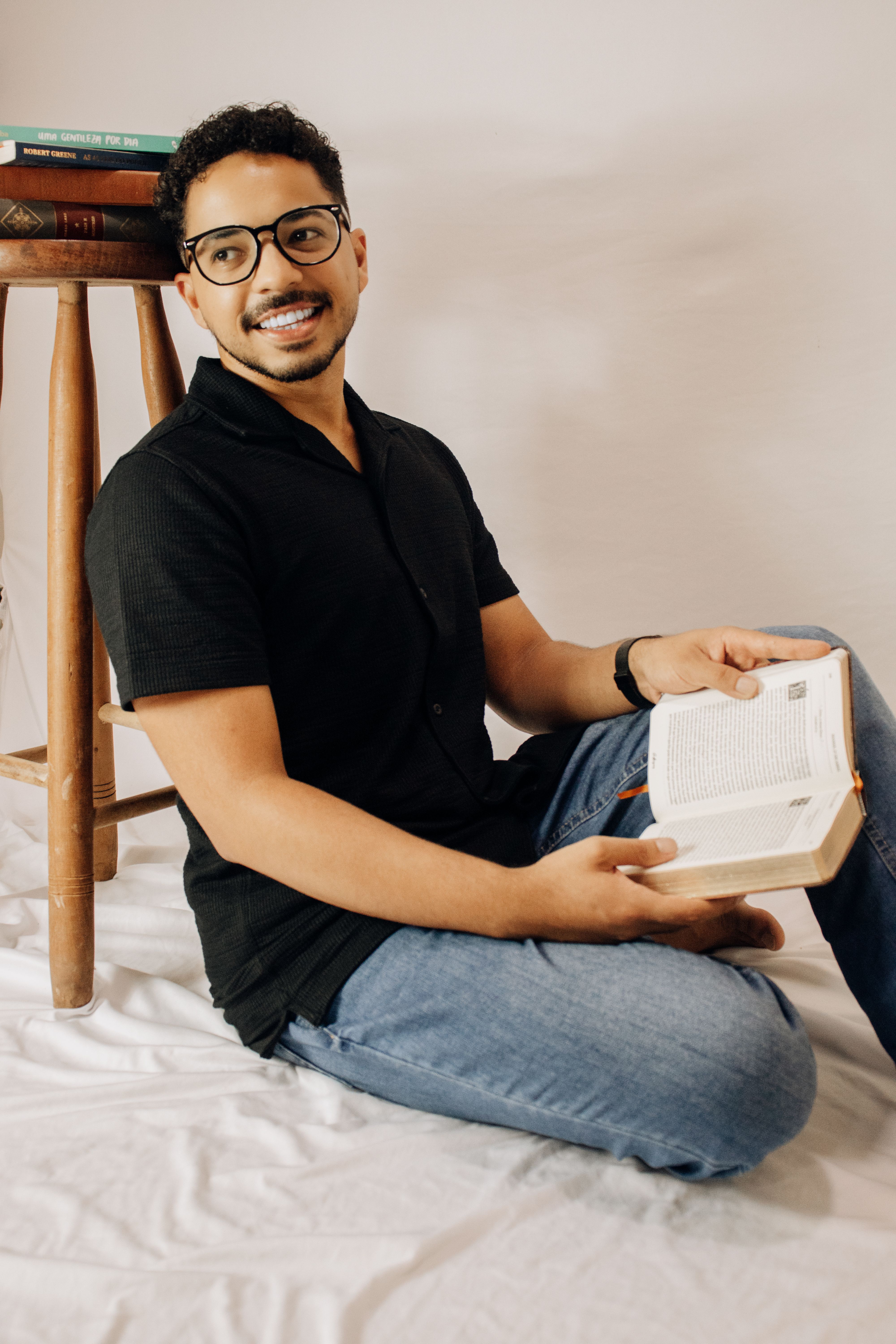 Man with glasses and mustache sitting indoors reading a book and smiling.