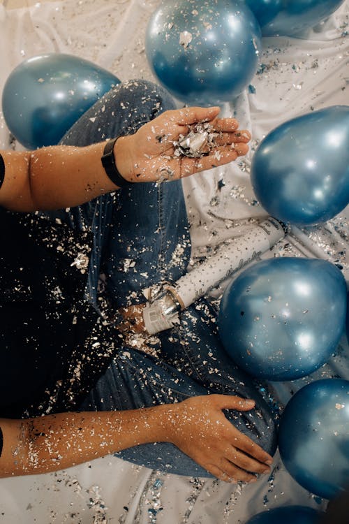 A person is holding blue balloons and confetti
