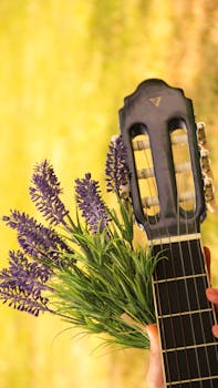 A close-up of a guitar head with lavender flowers against a bright summer field background.