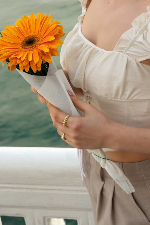 A woman holding a bouquet of flowers by the water