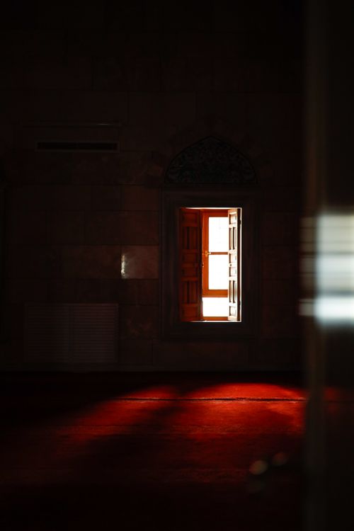 Free A serene mosque interior with warm light reflecting off a red carpet through an open window. Stock Photo