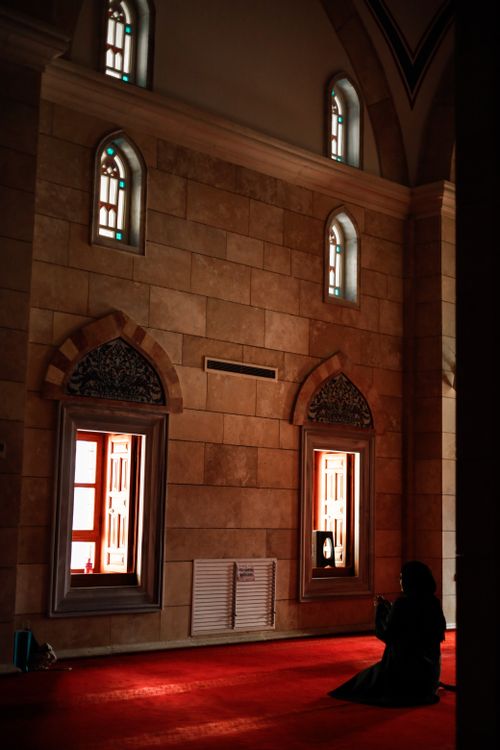 Free A woman in silhouette prays in a peaceful mosque interior with red carpets and arched windows. Stock Photo
