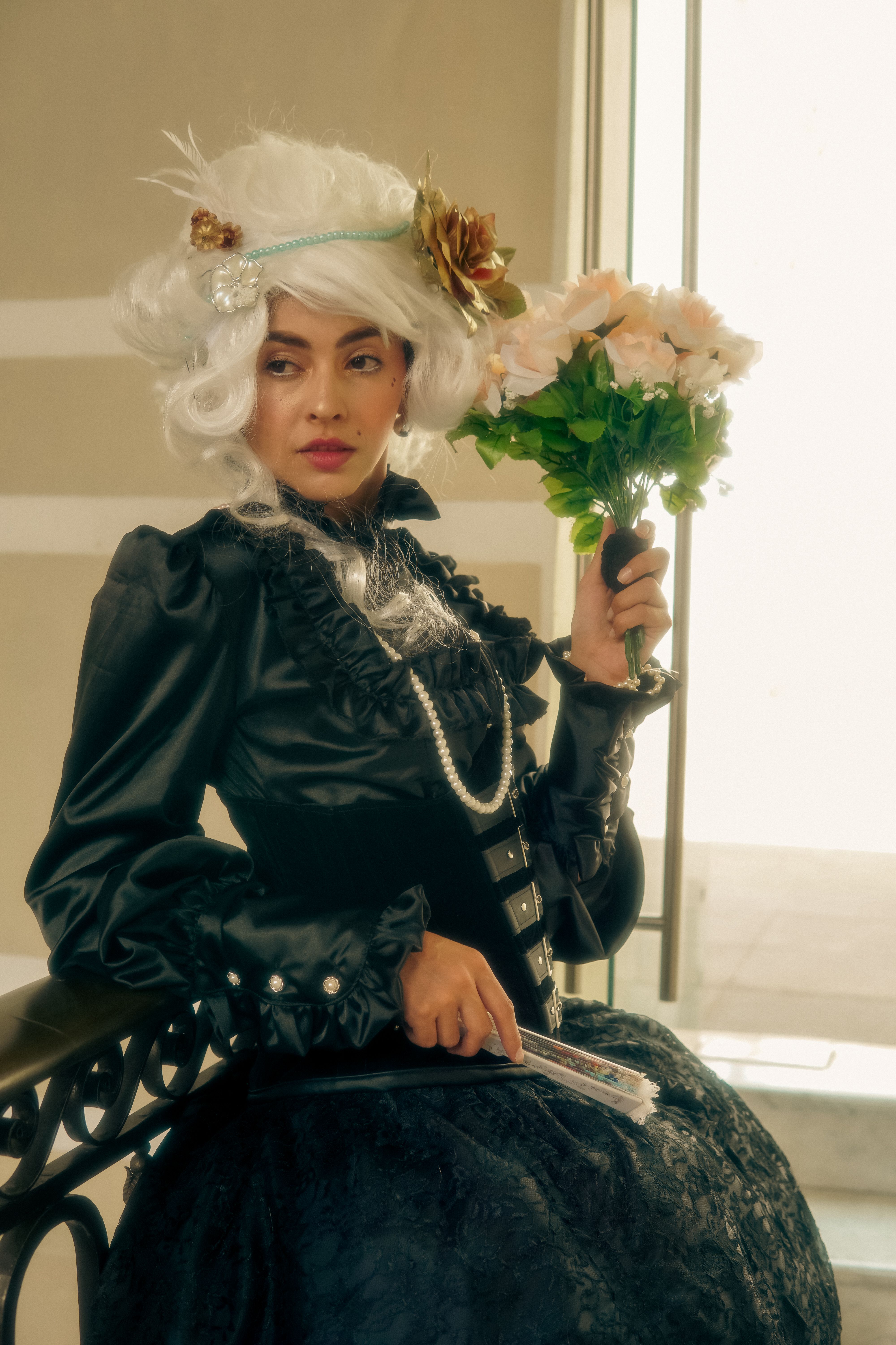 A stylish woman in vintage attire posing with a bouquet indoors.