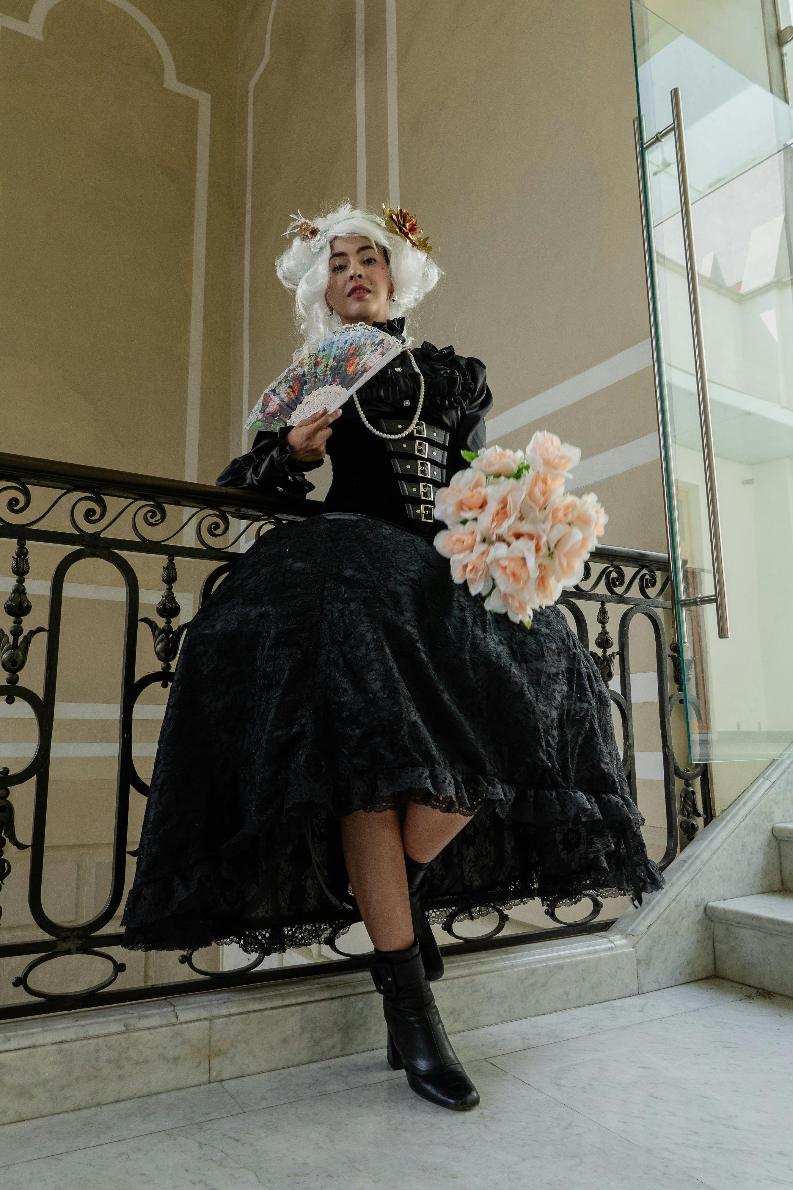 Victorian-inspired portrait of a woman in costume, posed with a fan and flowers indoors.