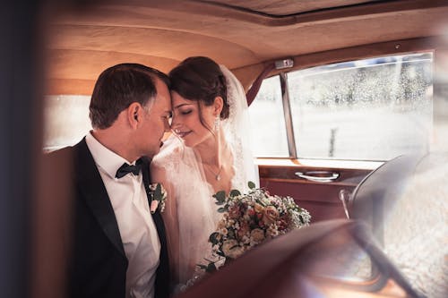 A bride and groom in the back seat of a vintage car