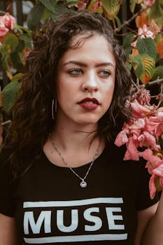 一位留着卷发的时尚年轻女子在户外粉红色花丛中摆姿势