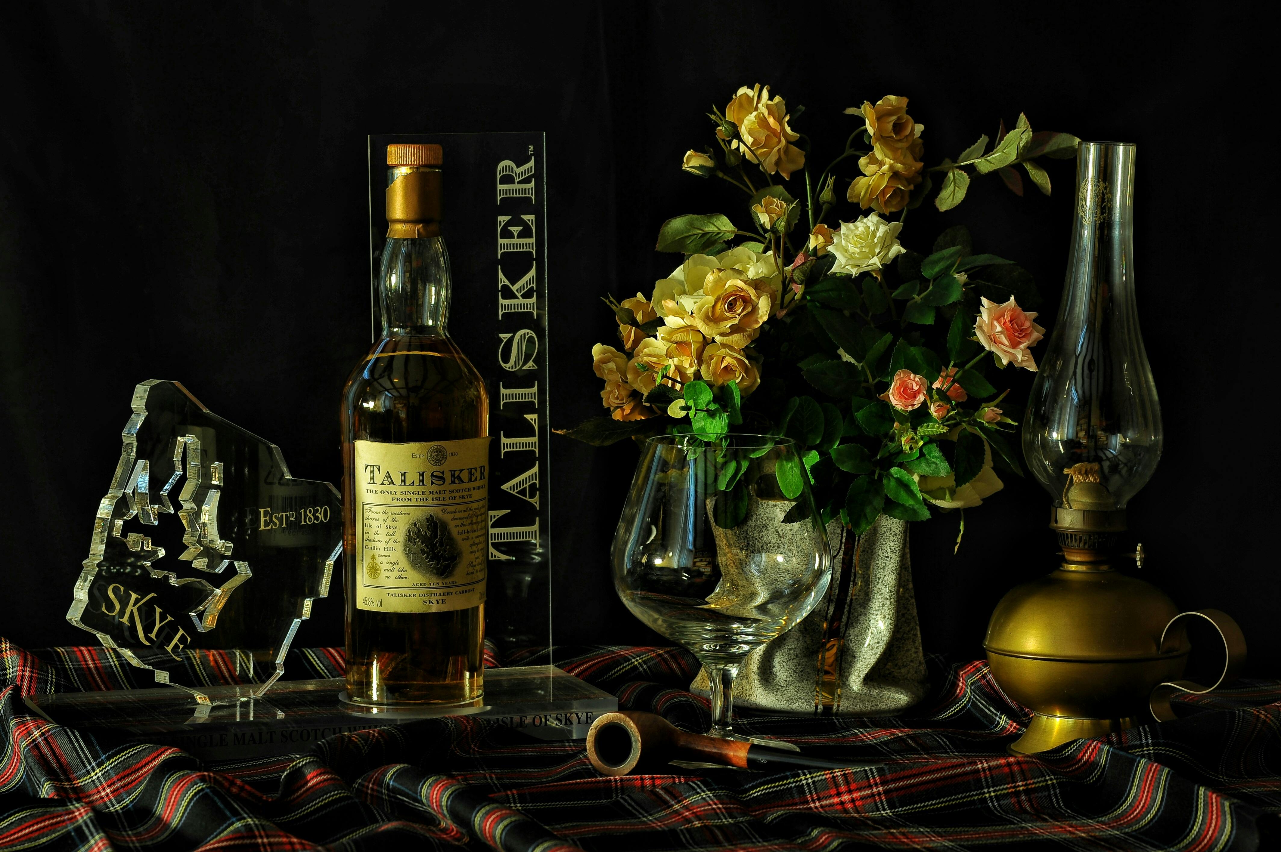 yellow and pink roses in vase beside wine bottle close up photography