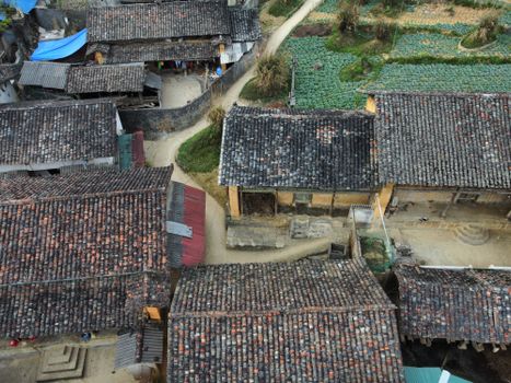 Aerial shot of a rustic village with traditional tiled roofs surrounded by farmland and pathways.
