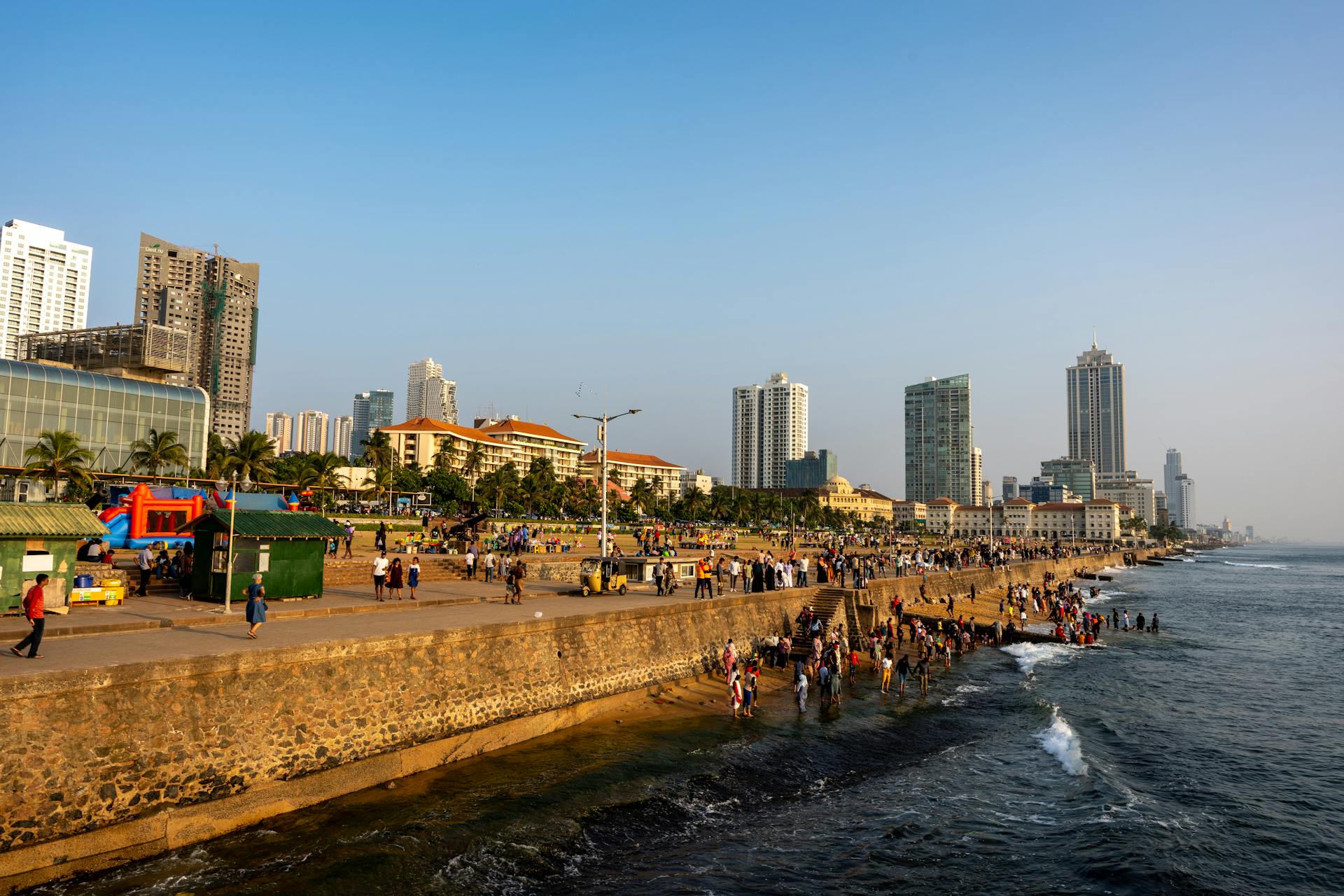 A vibrant view of Galle Face Green promenade in Colombo, Sri Lanka, with people enjoying the seaside and urban skyline.