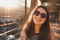 一位戴着太阳镜的年轻女子微笑着，沐浴在户外温暖的日落光芒中