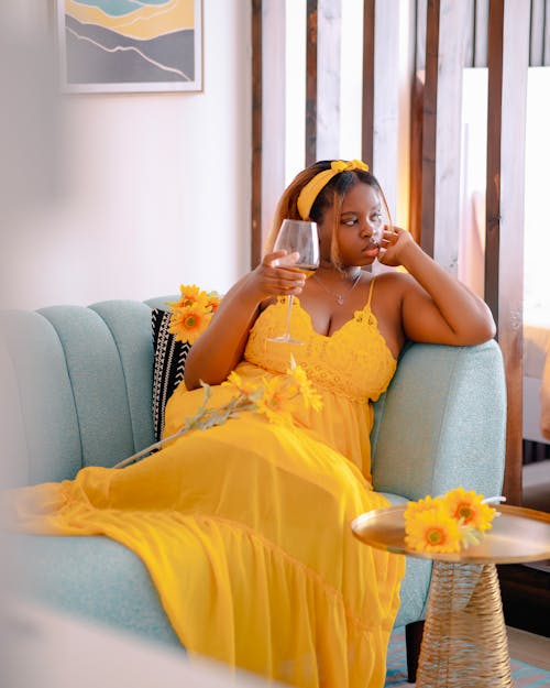 A woman in a yellow dress is sitting on a couch