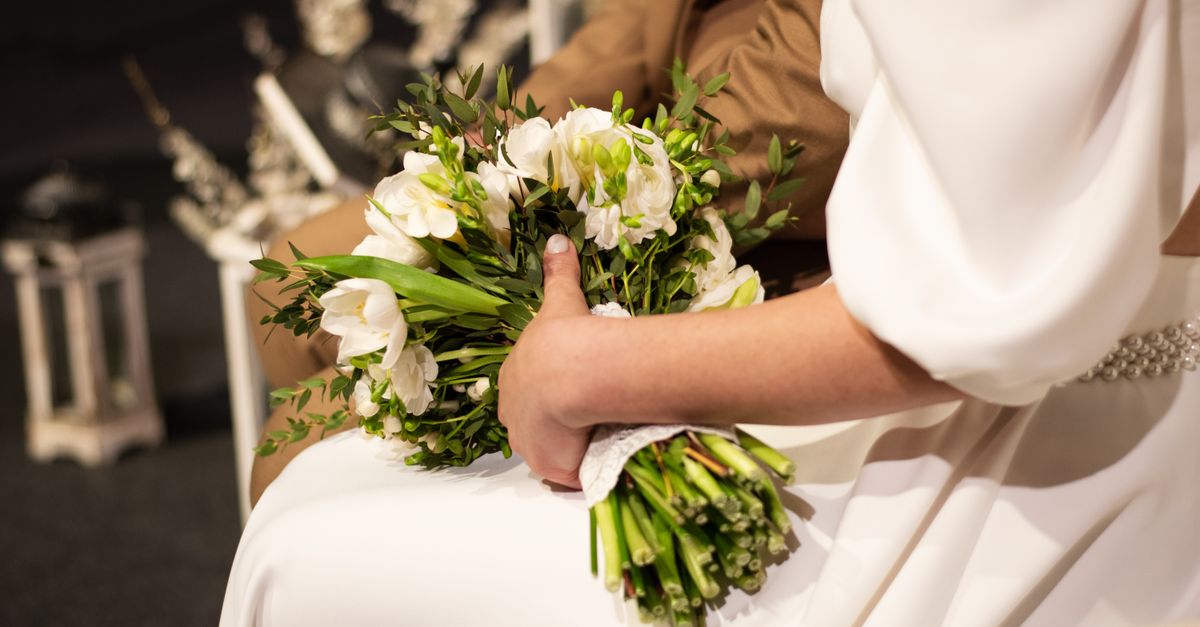Close-up of a bride holding a lush bouquet on her wedding day, seated beside the groom.