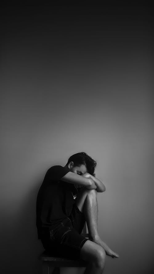 Free Grayscale Photography of Man Sitting Beside Wall Stock Photo