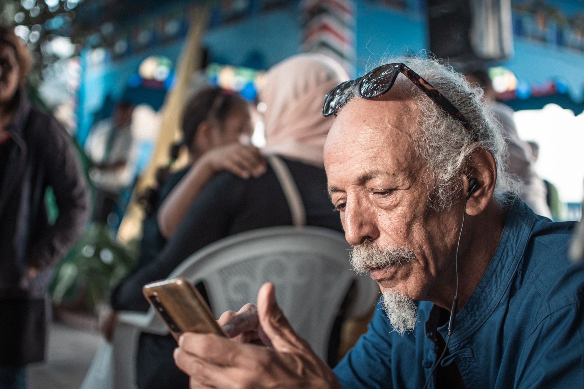 An elderly man with gray hair and sunglasses uses his smartphone outdoors in La Marsa, Tunisia.