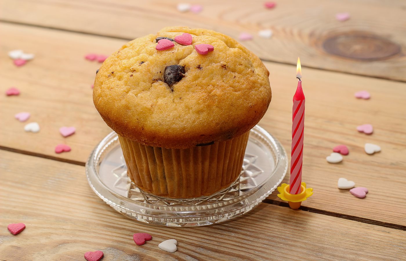 Celebrate with a sweet muffin and a single lit candle, surrounded by heart confetti.