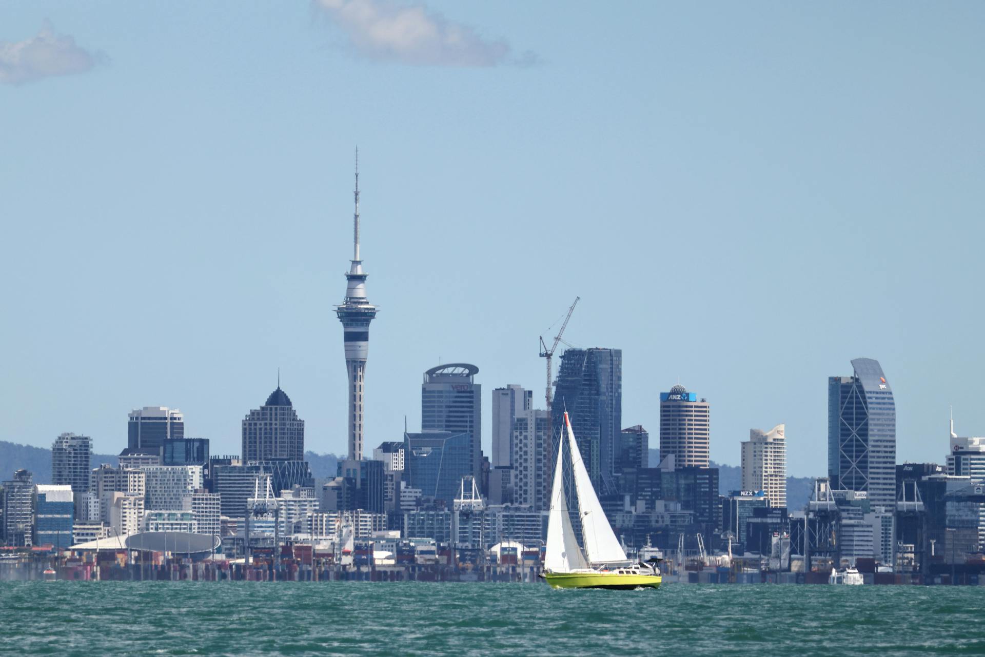 Sailboat navigating the waters with Auckland skyline, featuring the Sky Tower, in the backdrop.