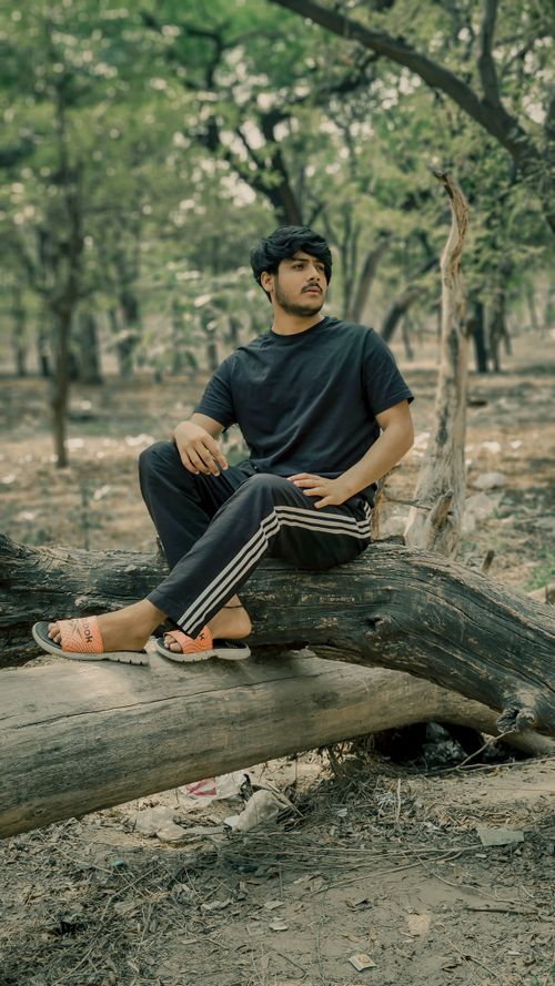 Free Man sitting on a tree trunk in a forest, wearing casual attire, capturing a moment of relaxation outdoors. Stock Photo