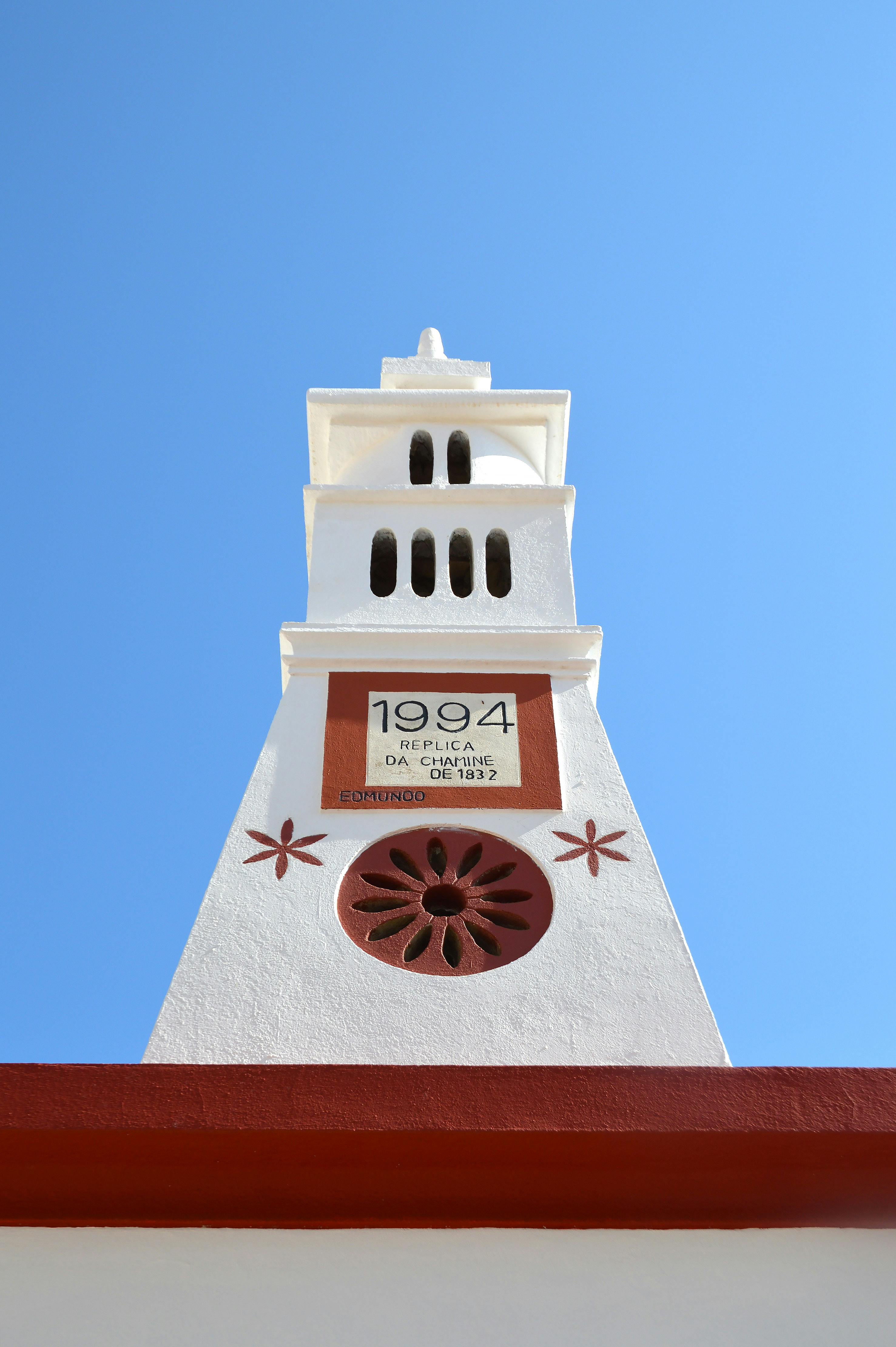 Low angle view of a historic tower in Alte, Portugal with a clear blue sky backdrop.