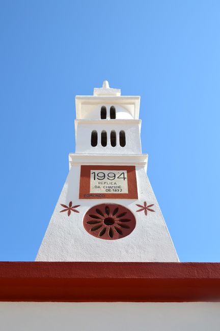 Low angle view of a historic tower in Alte, Portugal with a clear blue sky backdrop.