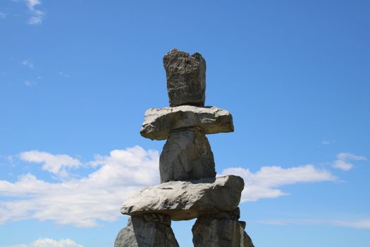 Stone inukshuk sculpture set against a vibrant blue sky and clouds in Vancouver.