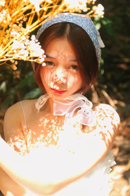 Free Elegant portrait of a woman under dappled sunlight with floral shadows, creating a serene ambiance. Stock Photo