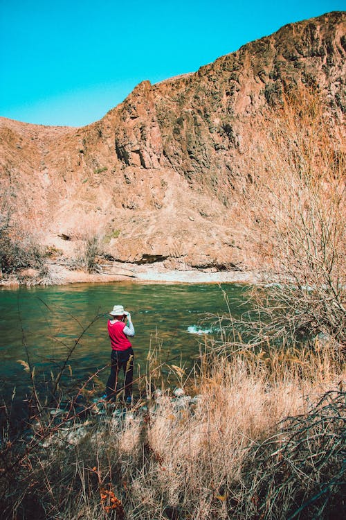 Person in Red and Gray Long-sleeved Shirt Standing Near Body of Water