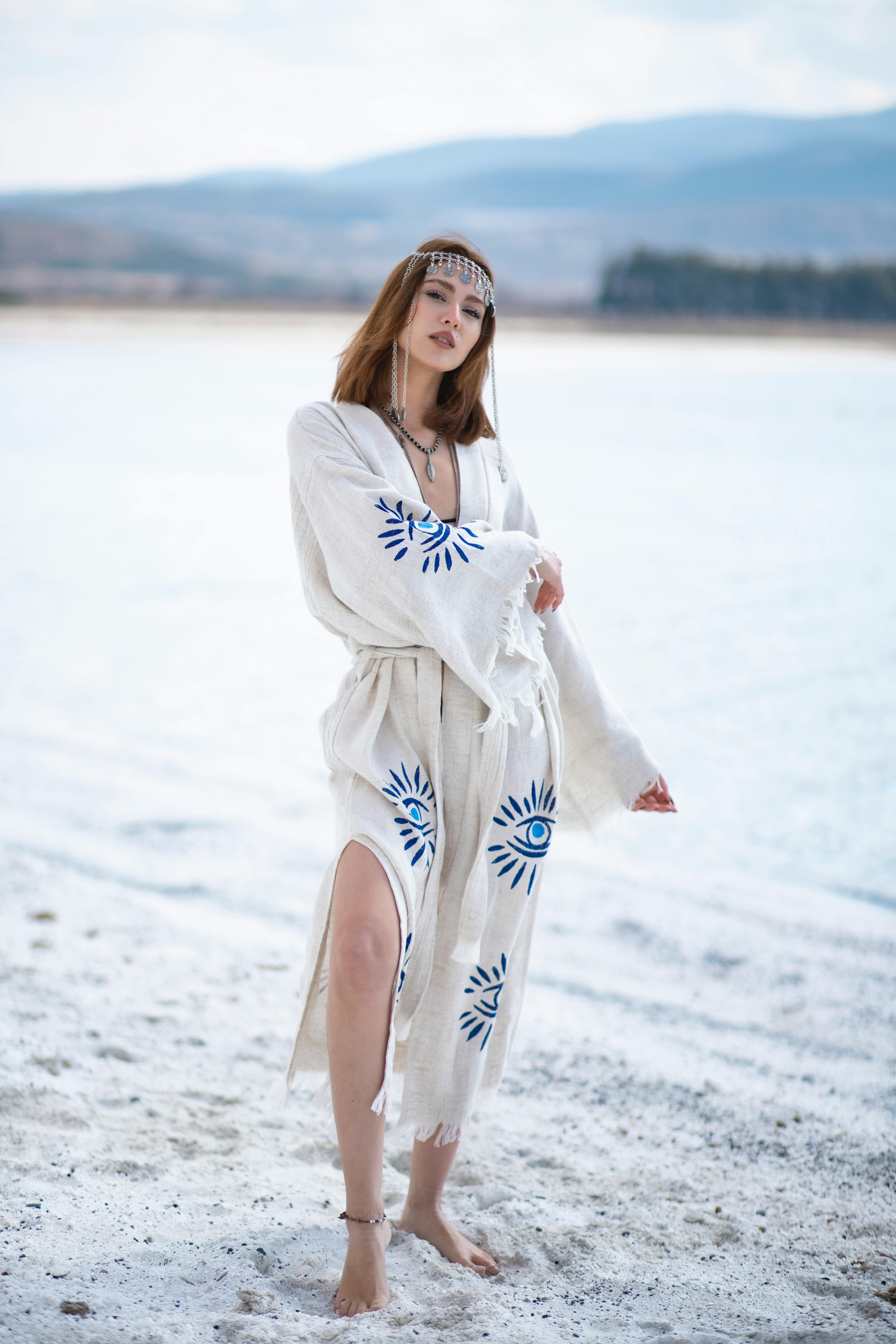 A bohemian woman in an embroidered dress poses gracefully on a serene beach.