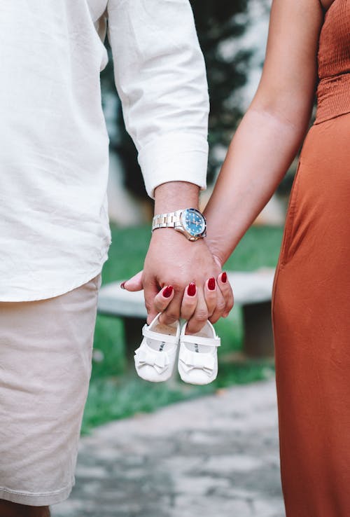 A couple holding hands and holding baby shoes