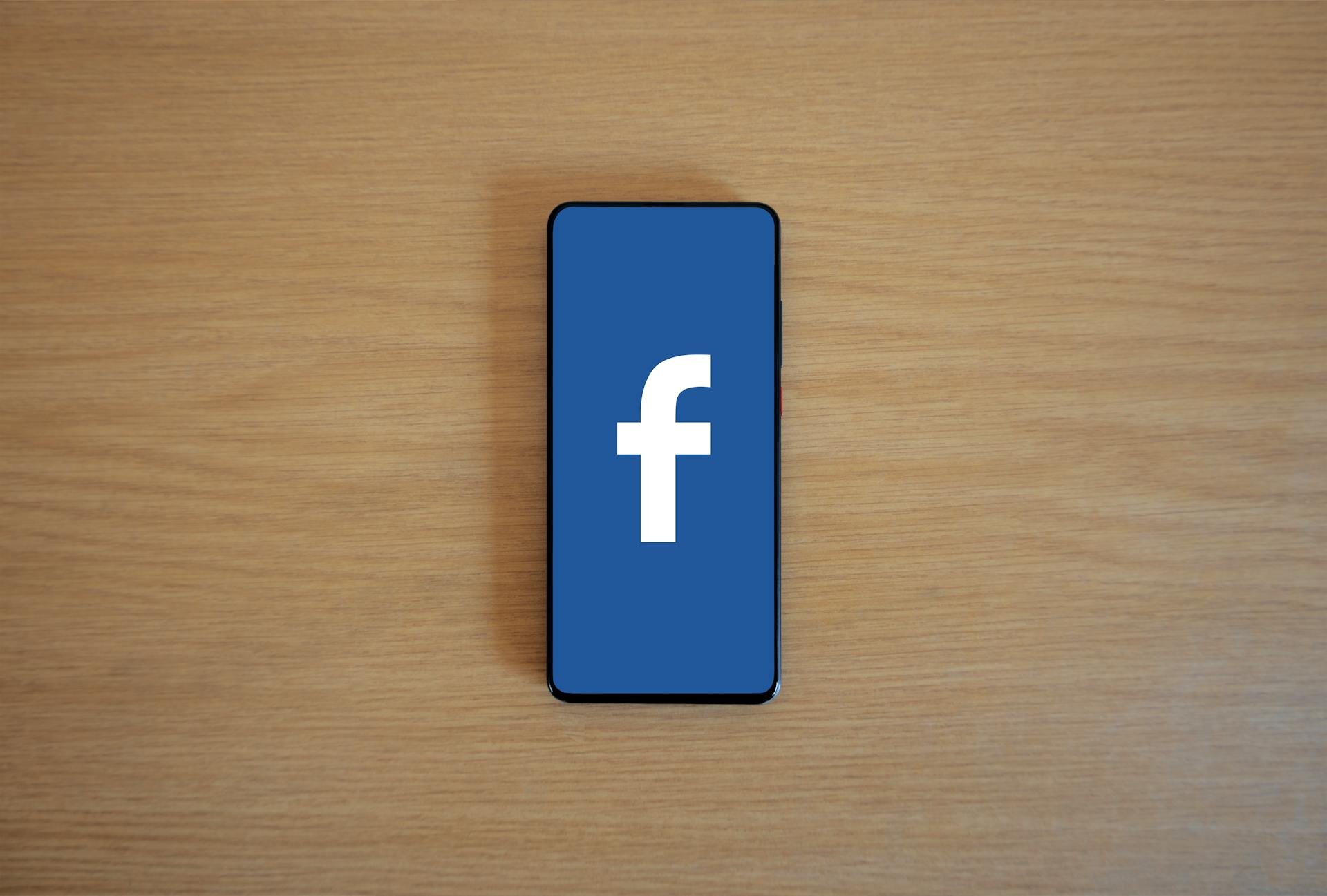 Smartphone with Facebook logo on screen, placed on a wooden background. Top view.