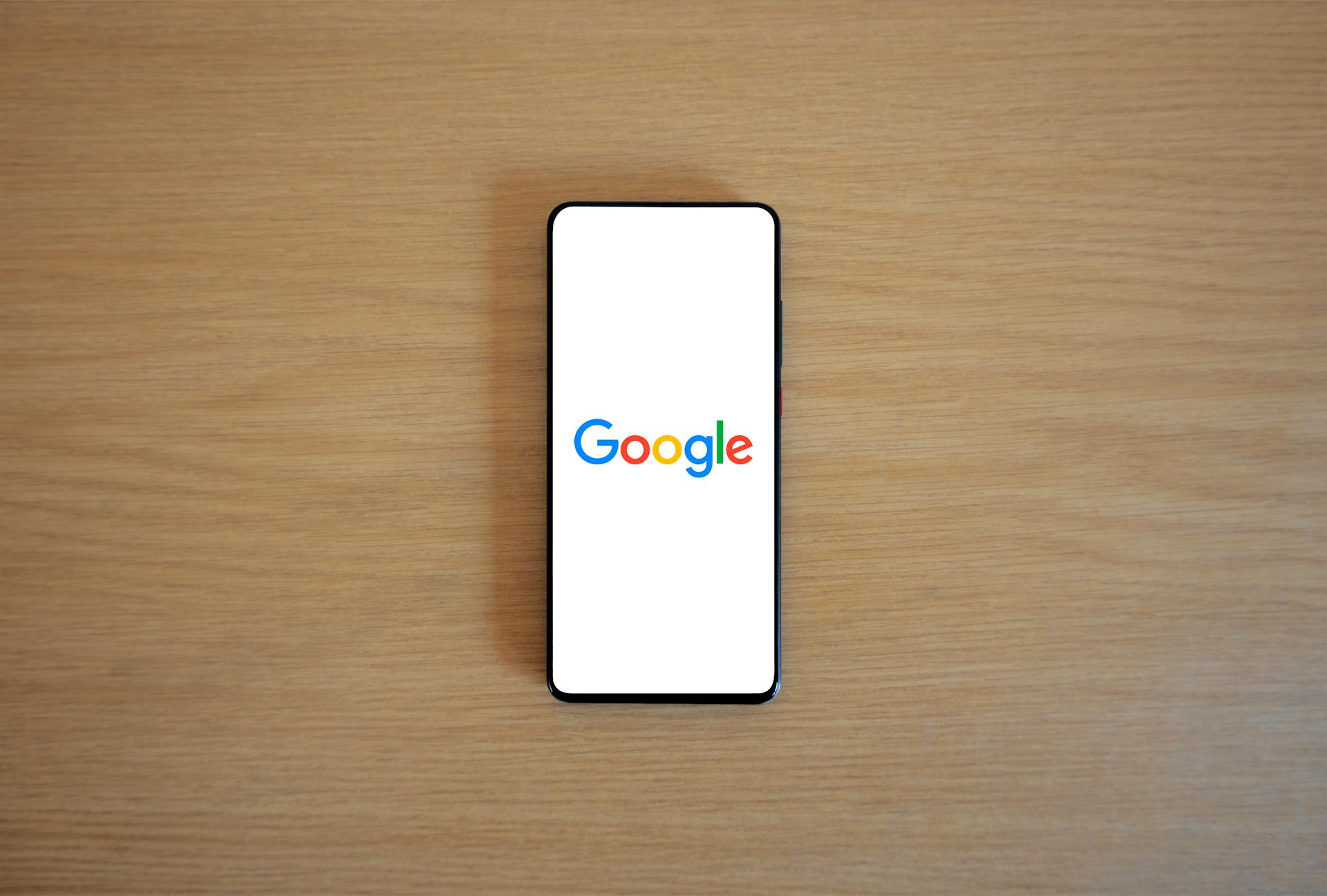 A smartphone displaying the Google homepage on a wooden surface, viewed from above.